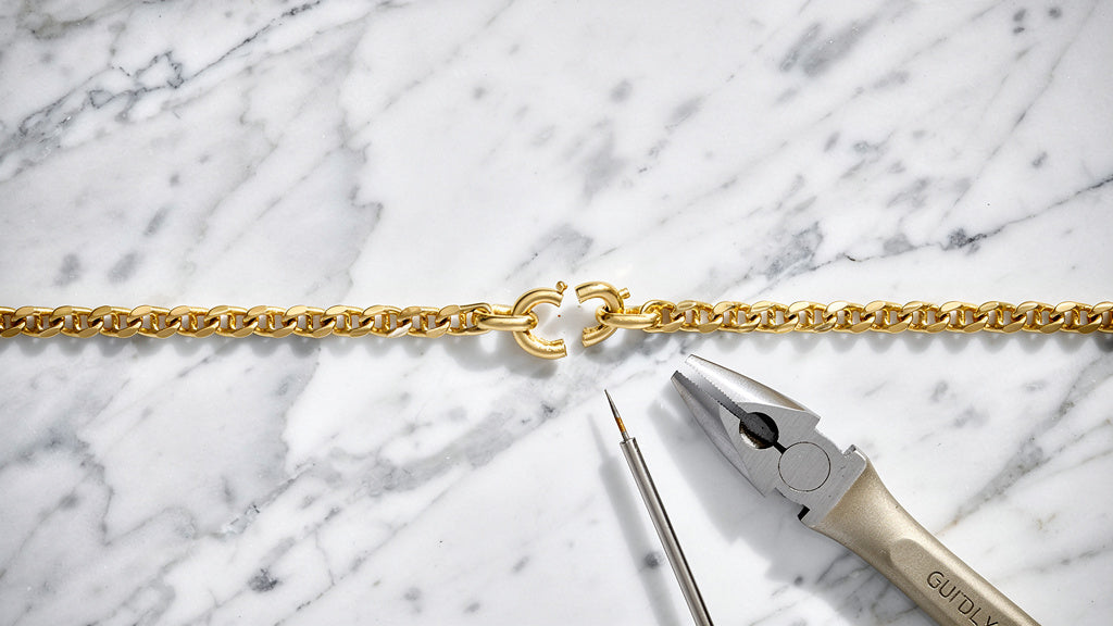 Broken gold chain with open link beside jeweler's tools for gold jewelry repair