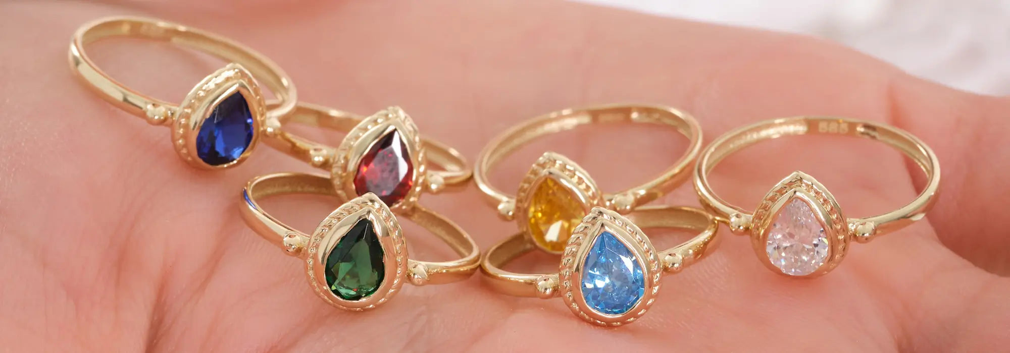 Gold rings with pear-shaped blue, red, green, yellow, and clear cubic zirconia on a hand