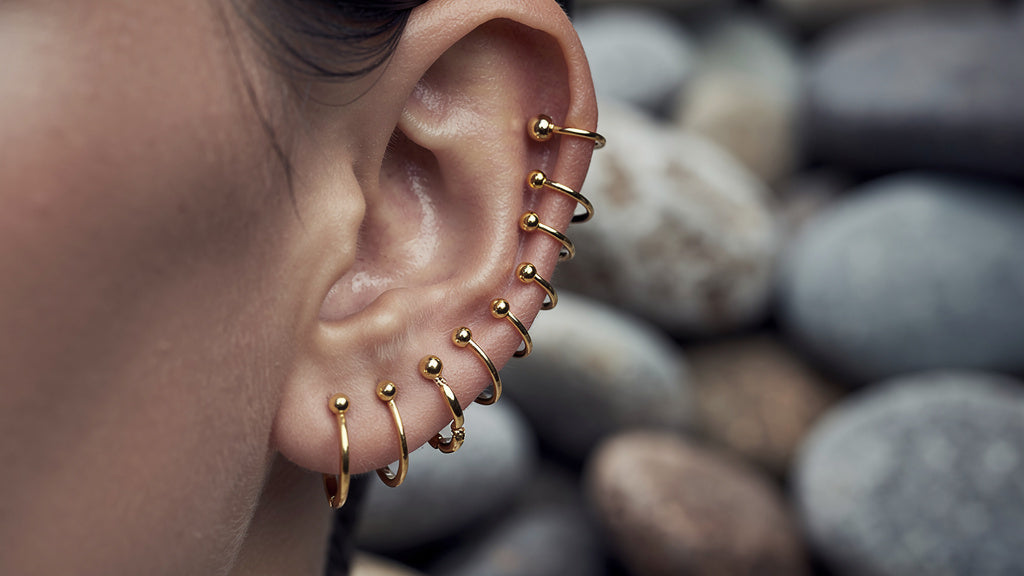 Ear with multiple gold earrings showing an ear piercing chart of lobe and cartilage placements