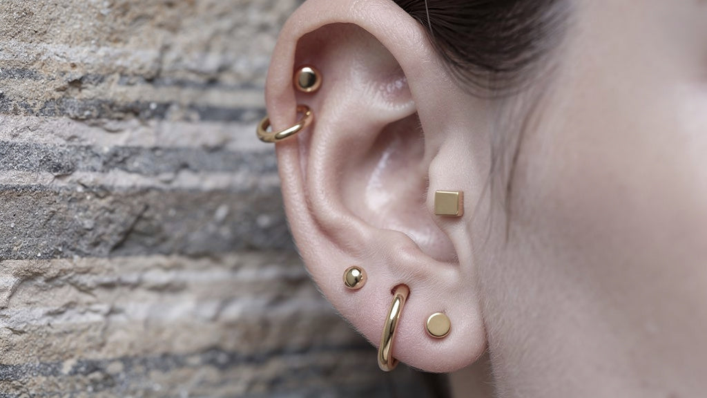 Ear with different ear piercings in the lobe and cartilage, styled with small gold studs and hoops