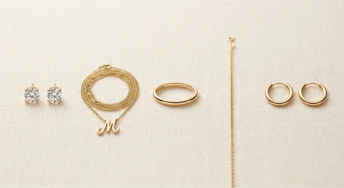 Five essential 14K gold jewelry pieces - studs, chain, ring, bracelet, hoop - on cream linen