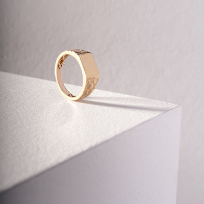 Signet gold ring on a light gray surface with soft shadows