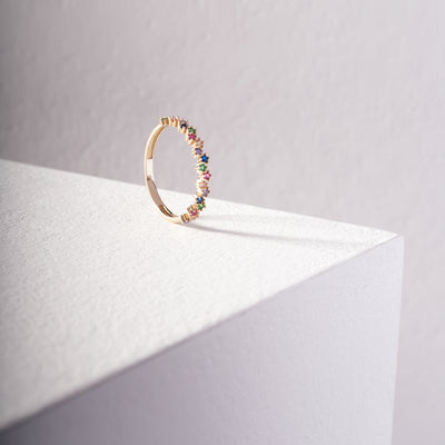 Gold ring with colorful gemstones on a light gray background