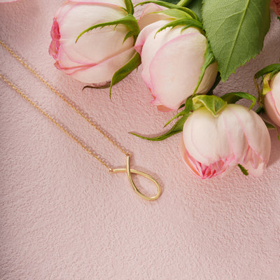 Gold necklace with a unique pendant on a pink surface with pink flowers.
