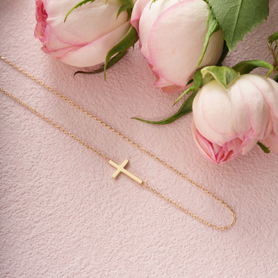 Gold necklace with a cross pendant on a pink surface with pink roses.