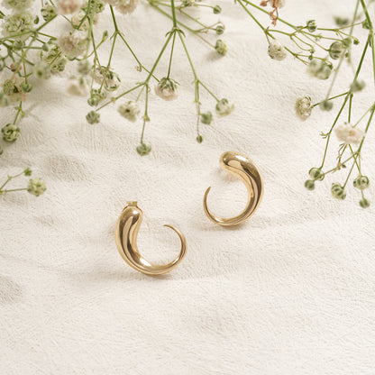 Gold hoop earrings on a white fabric background with small flowers.