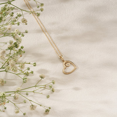 Gold heart-shaped necklace on a soft beige background with delicate flowers.