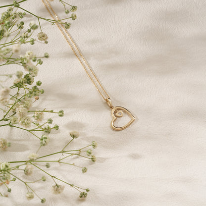 Gold heart-shaped necklace on a soft beige background with delicate flowers.