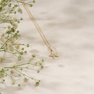 Gold star-shaped necklace on a light beige background with delicate flowers.