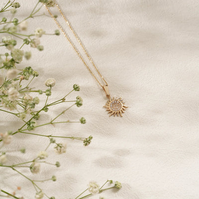 Gold necklace with a sun pendant on a light fabric background