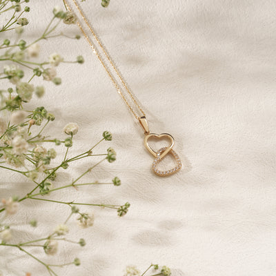 Gold necklace with a heart-shaped pendant on a light fabric background with small flowers.