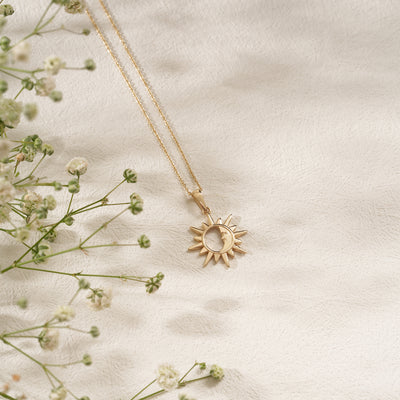 Gold sun-shaped pendant necklace on a light fabric background with delicate flowers.