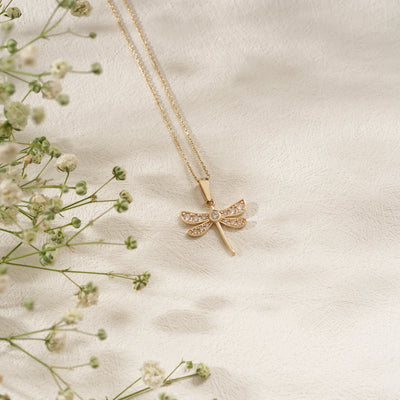 Gold necklace with a dragonfly pendant on a soft beige background with delicate flowers.