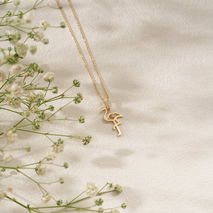 Gold flamingo pendant necklace on a light background with delicate flowers