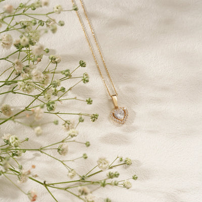 Gold necklace with a heart-shaped pendant on a light background with small flowers.