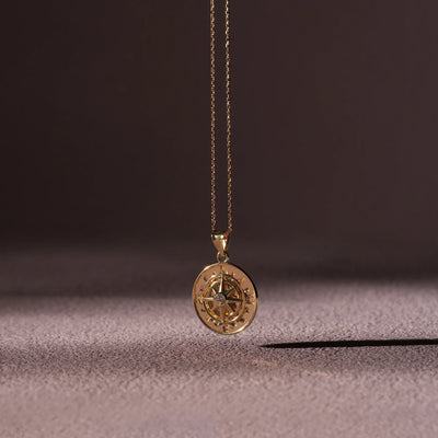 Gold compass pendant necklace on a textured surface with a dark background