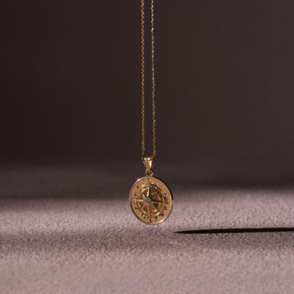 Gold compass pendant necklace on a textured surface with a dark background