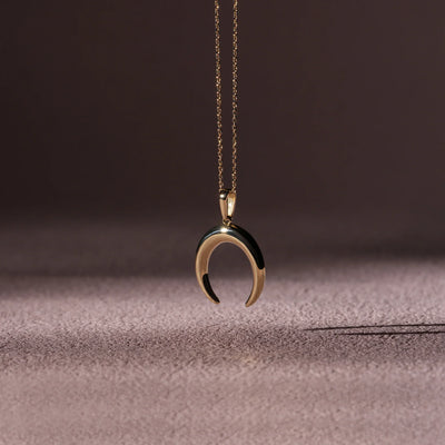 Gold crescent moon necklace on a textured surface with a dark background