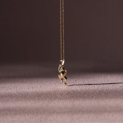 Gold frog pendant necklace on a dark fabric background