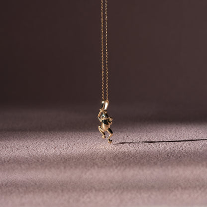 Gold frog pendant necklace on a dark fabric background