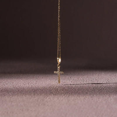 Gold cross necklace on a textured surface with a dark background