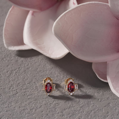 Gold earrings with red gemstones on a gray surface with pink flowers.