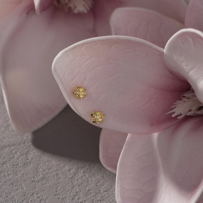 Yellow gold stud earrings with round gemstones displayed on pink flower petals
