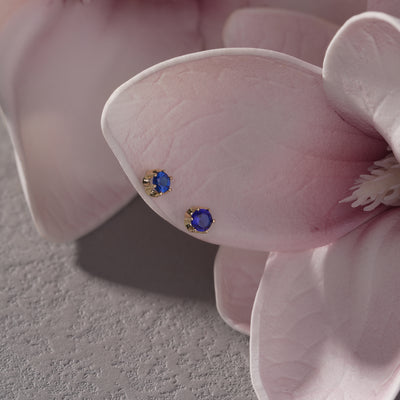 Gold stud earrings with blue gemstones displayed on pink flower petals
