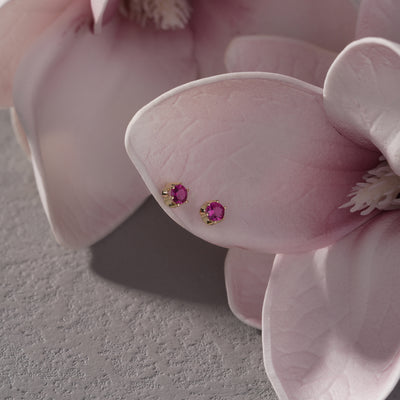 Gold stud earrings with round pink gemstones displayed on soft pink flower petals
