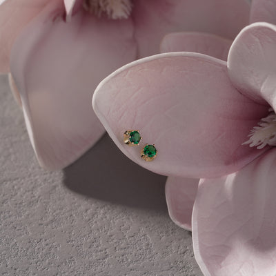 Gold stud earrings with green gemstones on pink flower petals, elegant jewelry closeup