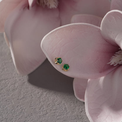 Pair of emerald green gemstone earrings on a pink orchid.