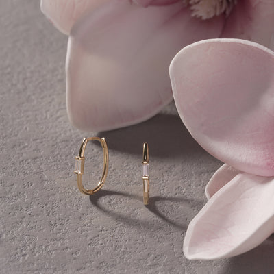 Two gold hoop earrings on a gray surface with pink petals in the background