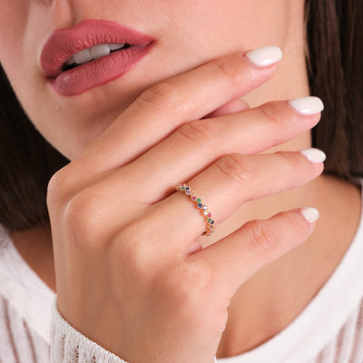 Close-up of a hand wearing a ring with colorful gemstones, held near the face.