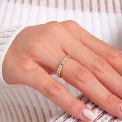 Hand wearing a gold ring with colorful gemstones on a white background