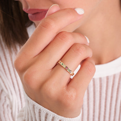 Close-up of a hand wearing a ring with colorful stones, against a blurred background.