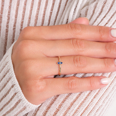 Hand wearing a gold ring with a blue eye design on a white background