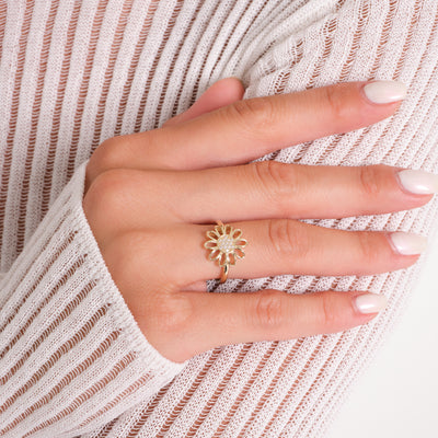 Hand wearing a gold sunflower ring on a white and pink striped fabric background