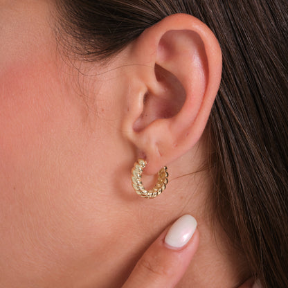 Close-up of an ear wearing a gold hoop earring with a blurred background