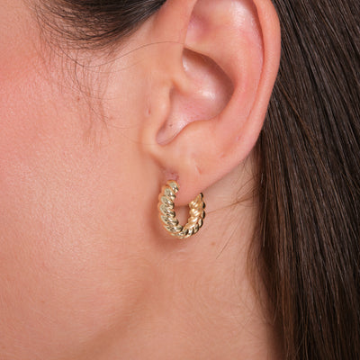 Close-up of a woman's ear wearing a twisted gold hoop earring