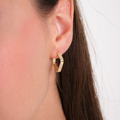 Gold hoop earring worn by a person with a neutral background