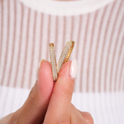 Hand holding gold hoop earrings with pavé diamonds, close-up jewelry detail