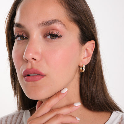 Close-up of a woman wearing gold hoop earrings with a plain background