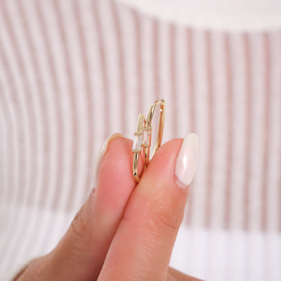 Gold hoop earrings held between fingers against a neutral background
