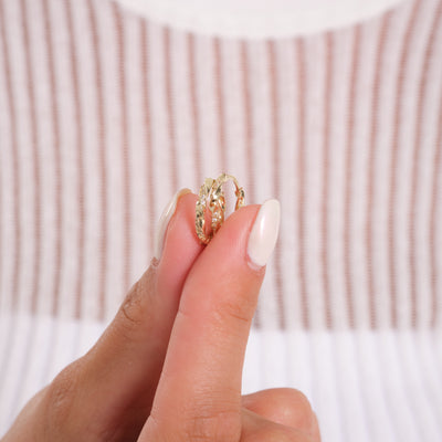 Hand holding gold textured hoop earrings with a striped background