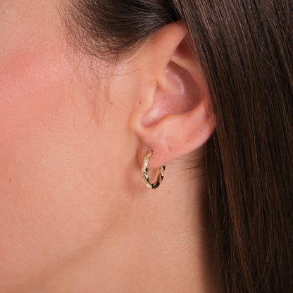 Close-up of an ear wearing a gold hoop earring with a neutral background
