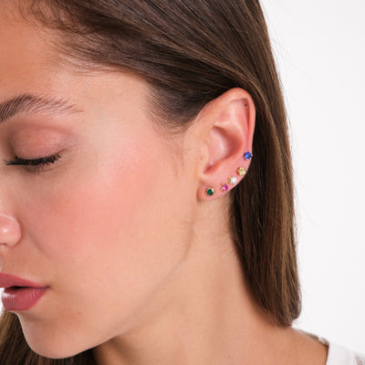 Woman wearing multiple gold stud earrings with colorful gemstones on ear