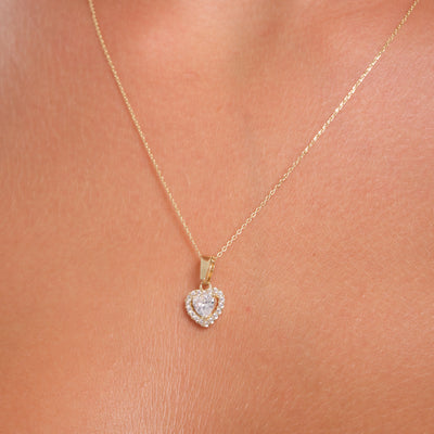 Gold necklace with a heart-shaped pendant on a person's neck