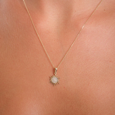 Gold necklace with a sunflower pendant on a person's neck