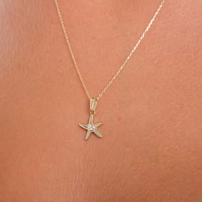 Gold starfish necklace on a person's neck against a pink background