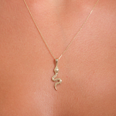 Gold snake pendant necklace on a person's neck against a pink background